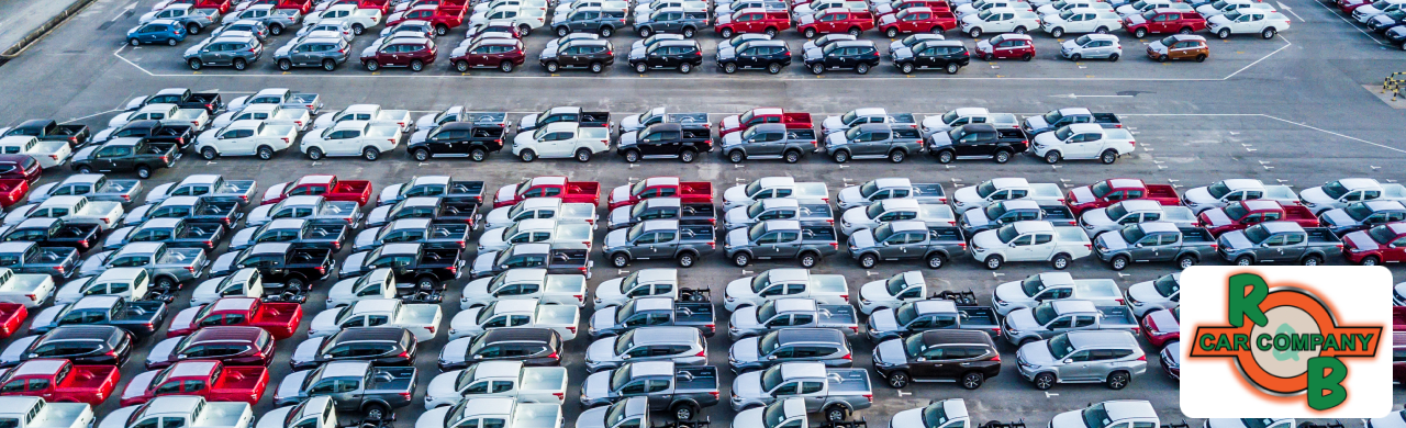 A large parking lot filled with rows of parked cars. The cars are arranged in neat lines, with the sun casting shadows across their surfaces.